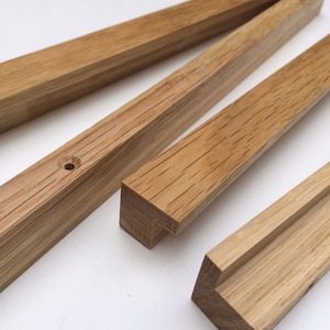 Könnte beinhalten: Nahaufnahme von mehreren unfertigen Holz-Bilderrahmen-Teilen. Die Teile sind rechteckig, mit natürlicher Holzmaserung und hellbrauner Farbe. Ein Teil hat ein vorgebohrtes Loch.