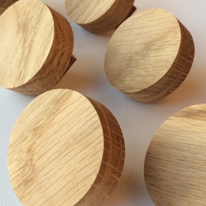 Puede incluir: Una colecci&oacute;n de pomos redondos de madera clara con un patr&oacute;n de vetas de madera natural. Los pomos son cil&iacute;ndricos con una parte superior e inferior planas y un borde ligeramente m&aacute;s oscuro. Probablemente son para muebles.