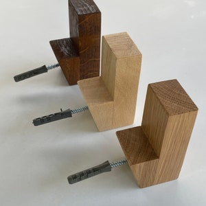 Peut inclure: Trois patères murales en bois de différentes teintes de marron et de bois naturel. Chaque crochet a une forme rectangulaire avec un petit rebord et comprend une vis et une cheville pour l'installation. Les crochets sont conçus pour suspendre des objets.