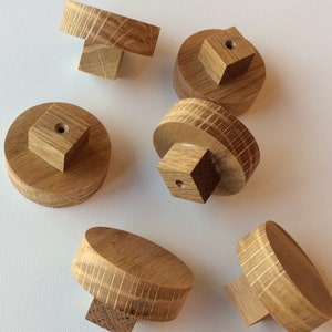 Puede incluir: Un conjunto de seis pomos de madera para armarios. Cada pomo es de color marr&oacute;n claro y presenta una parte superior redonda o rectangular con una base cuadrada. La veta de la madera es visible en cada pomo.