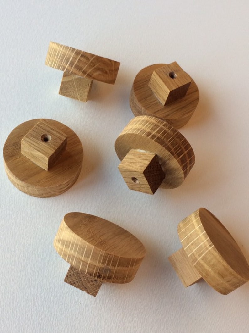 Puede incluir: Un conjunto de seis pomos de madera para armarios. Cada pomo es de color marr&oacute;n claro y presenta una parte superior redonda o rectangular con una base cuadrada. La veta de la madera es visible en cada pomo.