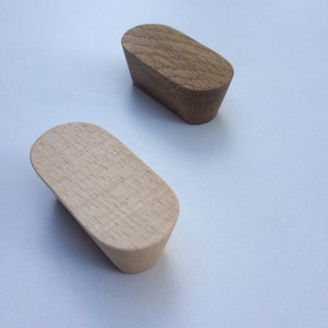 Può includere: Due pomelli in legno per mobili con parte superiore ovale e base rastremata. Un pomello è di colore chiaro, l'altro è marrone medio. I pomelli sono in legno e probabilmente per mobili.
