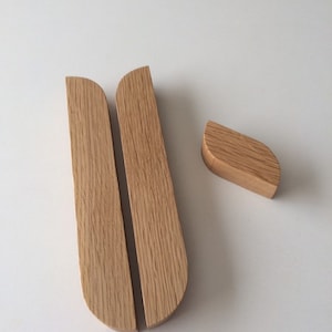 Peut inclure: Trois objets en bois sur une surface blanche. Deux sont grands, rectangulaires et incurvés en haut, avec une fente entre eux. Le troisième est une petite pièce en forme de feuille. Tous sont en bois clair.