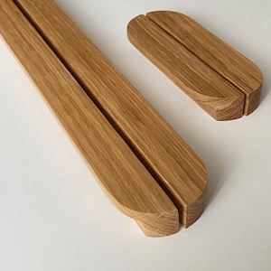Può includere: Due organizer da scrivania in legno. Uno è un lungo pezzo rettangolare con un'incisione al centro, e l'altro è un rettangolo più piccolo e arrotondato con un'incisione simile. Entrambi sono in legno marrone chiaro.