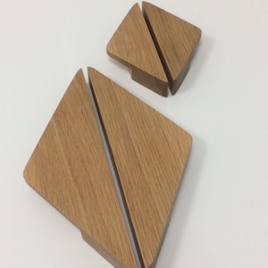 Può includere: Due set di sottobicchieri in legno, ciascuno composto da due pezzi triangolari ad incastro. I sottobicchieri sono realizzati in legno marrone chiaro con un motivo a venature visibile. Il design è moderno e minimalista, adatto a vari stili di arredamento.