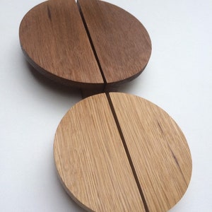 Può includere: Due oggetti in legno a forma di semicerchio. Uno è di colore marrone scuro e l'altro marrone chiaro. Ognuno ha una scanalatura verticale al centro. Gli oggetti sembrano decorativi o funzionali.