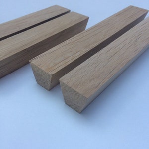 May include: Four unfinished, light brown wooden blocks with a square cross-section. The wood grain is visible on the surface. The blocks are arranged in a row, with two blocks in the foreground and two in the background.