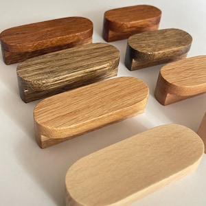 Könnte beinhalten: Eine Sammlung von oval geformten Holzobjekten in verschiedenen Braun- und Beigetönen. Die Objekte haben eine glatte, polierte Oberfläche und einen rechteckigen Sockel. Die Holzmaserung ist auf einigen Teilen sichtbar. Die Objekte sind auf einer weißen Oberfläche angeordnet.