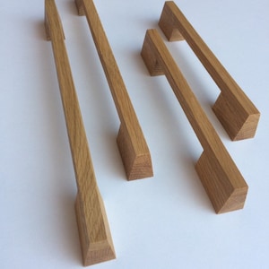 Può includere: Quattro maniglie per mobili in legno di colore marrone chiaro. Due sono lunghe e rettangolari, e due sono più corte. Le maniglie hanno un design moderno e geometrico, con una base rettangolare e un'impugnatura leggermente affusolata.