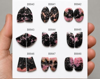 Puede incluir: Una colección de nueve pares de cabujones de rodonita pulidos dispuestos en un tablero blanco. Cada par está etiquetado con los códigos B9940 a B9948. Las piedras presentan un patrón moteado de inclusiones minerales negras y rosas variadas.