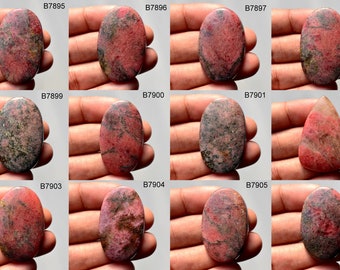 Puede incluir: Doce cabujones ovalados y en forma de lágrima de rodocrosita rosa y gris. Las piedras están colocadas en una mano para comparar el tamaño.