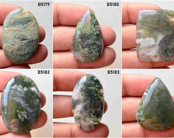 May include: Six green, white, and brown moss agate cabochons in various shapes, including oval, teardrop, and rectangular. The cabochons are displayed on a hand.