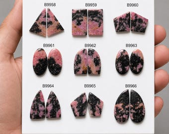 Puede incluir: Un tablero de presentación blanco con nueve pares de piedras preciosas de rodonita pulida en varias formas, incluyendo triángulos, rectángulos, óvalos y gotas. Cada par está etiquetado con los códigos B9958 a B9966, mostrando patrones rosas y negros.