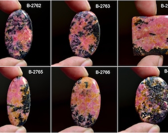 May include: Six oval and square shaped pink and black rhodochrosite cabochons. The stones have a variety of patterns and colors, including pink, black, and white.