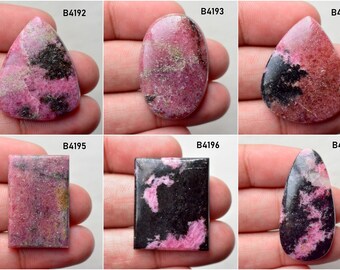 May include: Six cabochon cut rhodochrosite gemstones in various shapes, including oval, teardrop, and rectangular. The stones are a mix of pink and black with a speckled pattern.