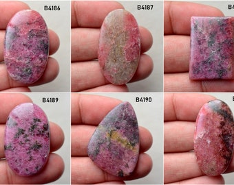 May include: Six oval and rectangular pink and gray cabochon gemstones with black flecks. The stones are labeled with the numbers B4186, B4187, B4188, B4189, B4190, and B4191.