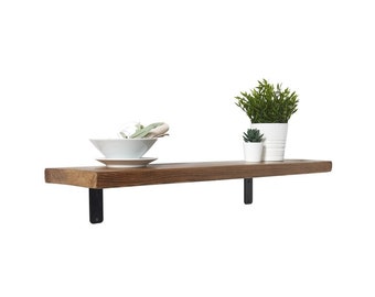 Puede incluir: Un estante de pared rectangular de madera con acabado de veta de madera marrón oscuro, sostenido por dos soportes metálicos negros en forma de L. Sobre el estante hay un cuenco blanco con tela, una maceta pequeña blanca y una maceta estriada.