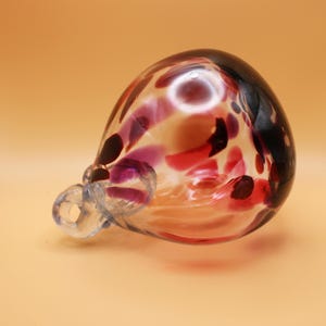 Puede incluir: Un adorno de vidrio con un acabado nacarado y un remolino de colores rojo, morado y negro.
