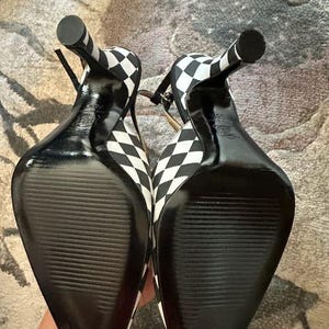 Puede incluir: Par de zapatos de tac&oacute;n alto con un estampado de cuadros blancos y negros. Los zapatos tienen punta afilada, finas correas en el tobillo y tac&oacute;n de aguja. Las suelas son negras con un dise&ntilde;o texturizado.