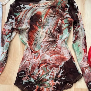 May include: A sheer, long-sleeved top with a brown background and a colorful Japanese-inspired print featuring fish, waves, and flowers.