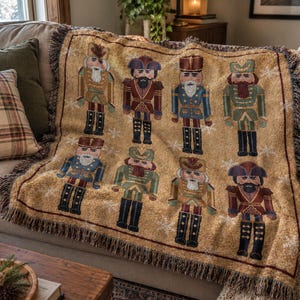 May include: A woven throw blanket in a tan color featuring a repeating pattern of eight nutcracker figures in various uniforms, including blue, green, and red accents, with small white snowflake motifs and a dark fringed border on all sides.