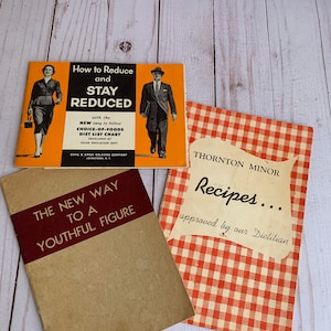 May include: Three vintage booklets on a light wood surface. The booklets include titles such as "How to Reduce and Stay Reduced" and "The New Way to a Youthful Figure." One booklet has a red and white checkered pattern.