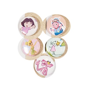 May include: Five colorful round buttons with cartoon characters. The buttons feature Dora the Explorer, Tinkerbell, a pink pig, a pink mouse, and the Pink Panther.