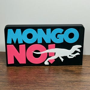 May include: A black rectangular sign with the words "MONGO NO!" in blue and pink, and a white dinosaur silhouette. The sign is on a wooden surface.
