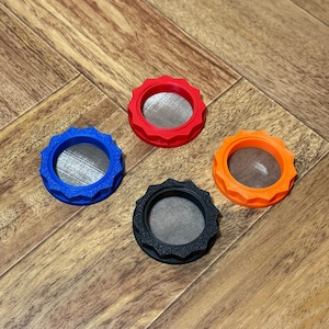 May include: Four colorful, circular objects with a textured, gear-like edge. The objects are in blue, red, orange, and black, each with a silver mesh center. They are arranged on a wooden surface.