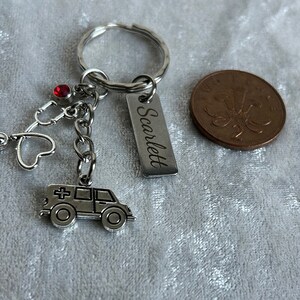 May include: Silver keychain with a red rhinestone, a stethoscope charm, a heart charm, an ambulance charm, and a silver tag engraved with the name "Scarlett".