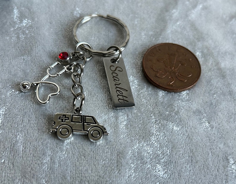 May include: Silver keychain with a red rhinestone, a stethoscope charm, a heart charm, an ambulance charm, and a silver tag engraved with the name "Scarlett".