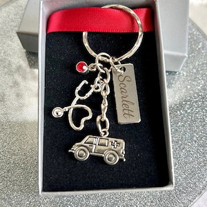 May include: A silver keychain with a red rhinestone, a stethoscope, a heart, and a small ambulance charm. The keychain also has a silver tag with the name "Scarlett" engraved on it.