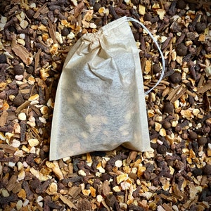 May include: A white muslin tea bag filled with a blend of dried spices and citrus peels, including orange peel, cinnamon sticks, cloves, and allspice berries.