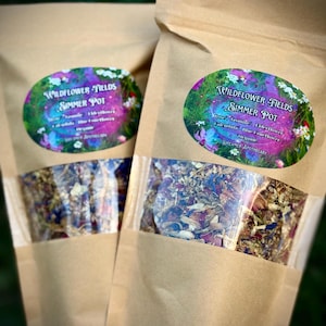 May include: Two brown paper bags with clear windows showing dried flower petals inside. The bags have labels that say "Wildflower Fields Simmer Pot" with a list of ingredients and "Dreamer Apothecary".