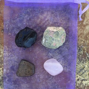 May include: Four tumbled stones in a purple mesh bag. The stones are black, brown, green and pink.