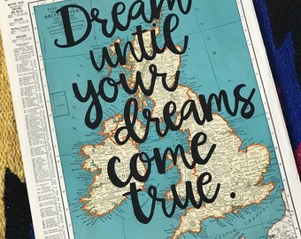 May include: A vintage map of the British Isles with the words "Dream until your dreams come true" in black script. The map has a blue-green ocean and tan landmasses. The page is from a World Atlas and Gazetteer.