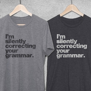May include: Two t-shirts with the text "I'm silently correcting your grammar." printed on them. The shirts are grey and dark grey.