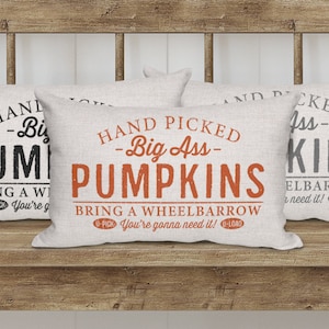 May include: Three decorative throw pillows with a linen texture. The pillows feature a fall-themed design with the text "Hand Picked -Big Ass- Pumpkins" and "Bring a Wheelbarrow You're gonna need it!" in black and orange.
