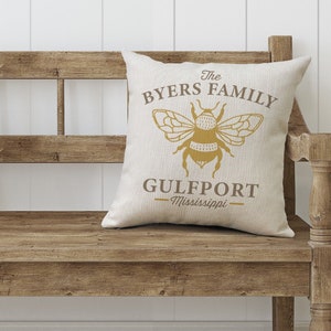 May include: A beige throw pillow with a brown bee graphic and the text "The Byers Family Gulfport - Mississippi".