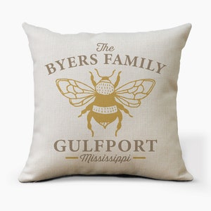May include: A beige throw pillow with the text "The Byers Family" and a bee illustration. Below the bee is the text "Gulfport - Mississippi".