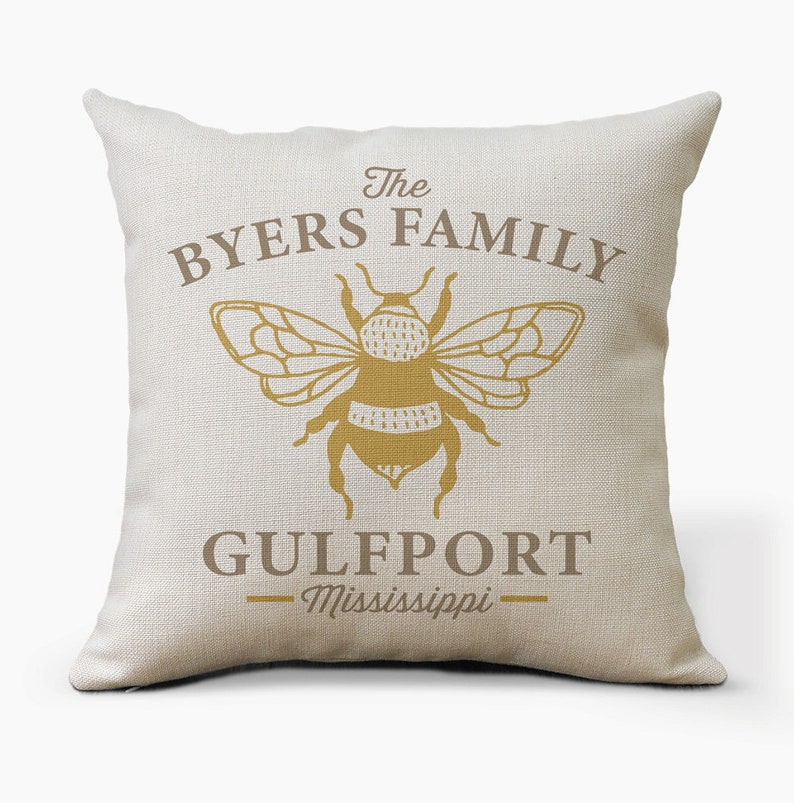 May include: A beige throw pillow with the text "The Byers Family" and a bee illustration. Below the bee is the text "Gulfport - Mississippi".