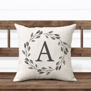 May include: A white throw pillow with a black and gray watercolor wreath design featuring the letter "A" in the center.