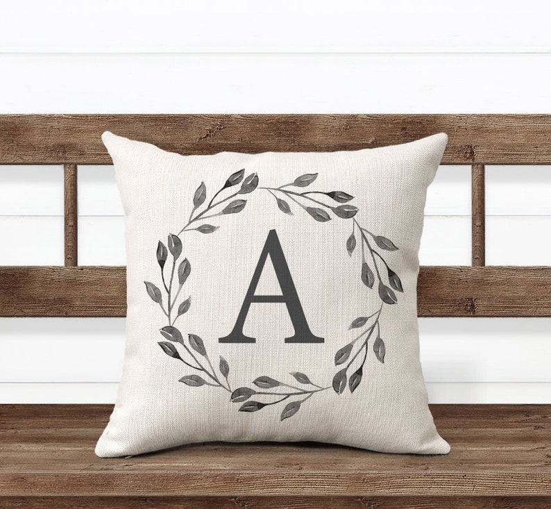 May include: A white throw pillow with a black and gray watercolor wreath design featuring the letter "A" in the center.