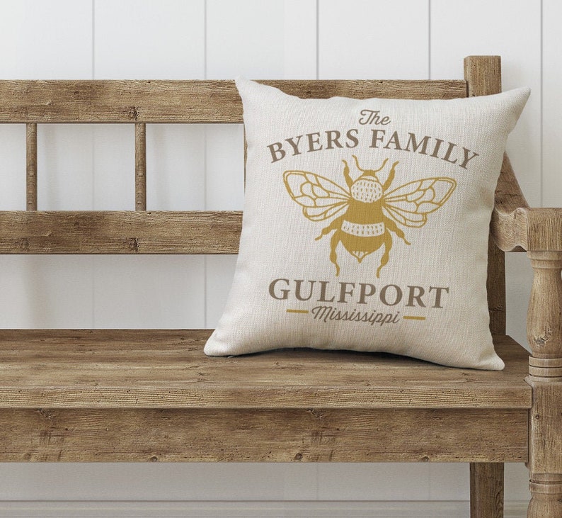May include: A beige throw pillow with a brown bee graphic and the text "The Byers Family Gulfport - Mississippi".