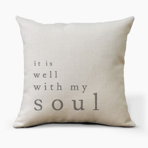 May include: A beige throw pillow with the text "it is well with my soul" printed in gray.