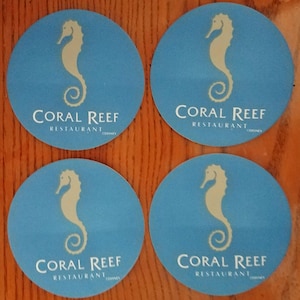 May include: Four round blue coasters with a white seahorse and the text "Coral Reef Restaurant" in white.