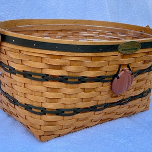 May include: A woven basket with black and green trim and a pumpkin-shaped charm. The basket has a label that reads "Longaberger Traditions Collection Family Harvest".