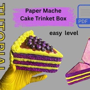 May include: A paper mache cake trinket box tutorial. The cake slice is yellow, purple, and brown with a blueberry topping. The text on the image says "Paper Mache Cake Trinket Box" and "easy level".