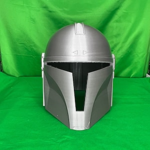 May include: A gray 3D printed helmet with a visor and a textured surface. The helmet is designed to resemble a Mandalorian helmet from the Star Wars franchise.