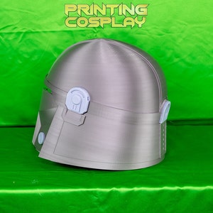 May include: A silver-colored helmet with a visor and ear pieces, likely for cosplay or costume use. The helmet has a smooth, metallic finish and is set against a bright green background. The text "PRINTING COSPLAY" is visible at the top.